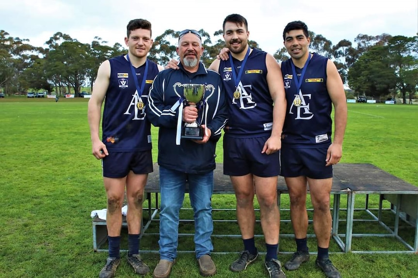 Four men stand next to each other, one holding a premiership cup 