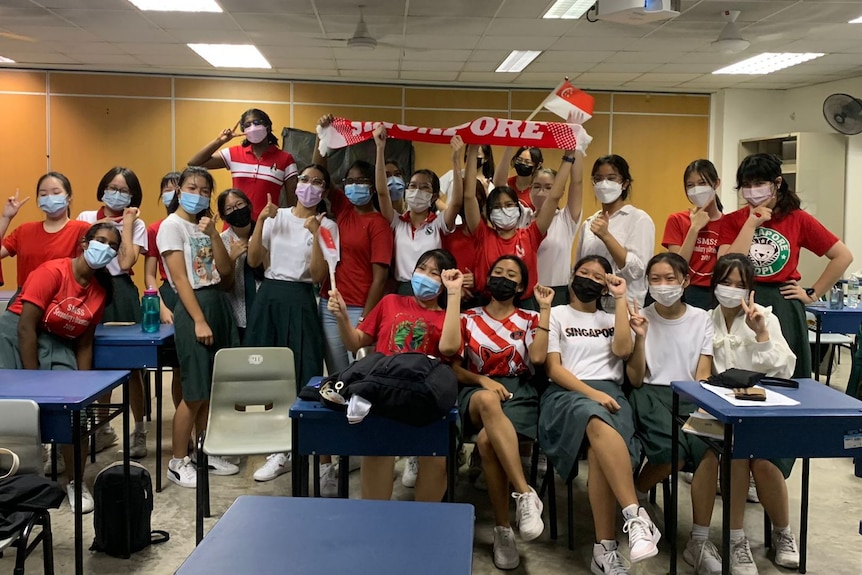 A group of students holding up the Singapore flag and dressed in red and white.
