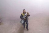 A distressed man holding an injured baby runs through the dust.