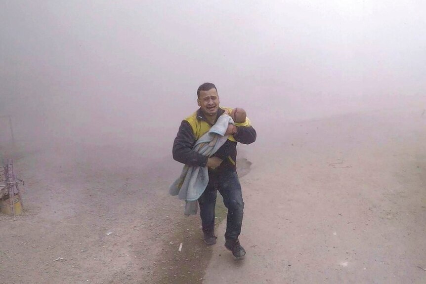 A paramedic carrying his wounded son flees from the scene of an attack after air strikes in Damascus.