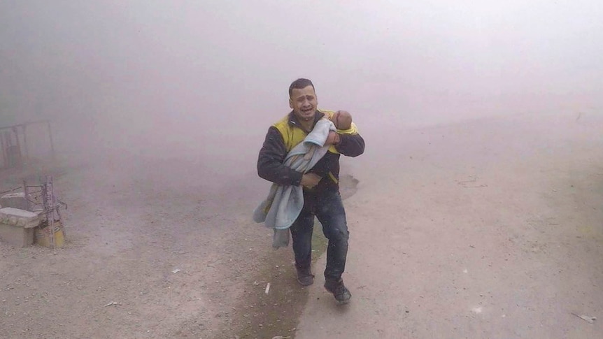 A paramedic carrying his wounded son flees from the scene of an attack after air strikes in Damascus.