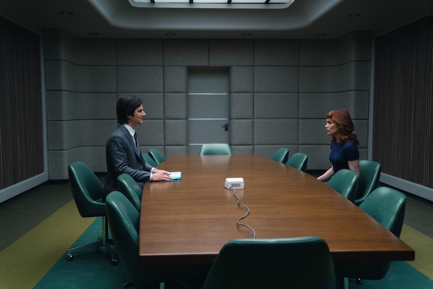 A man and woman sit across from each other in an office boardroom.