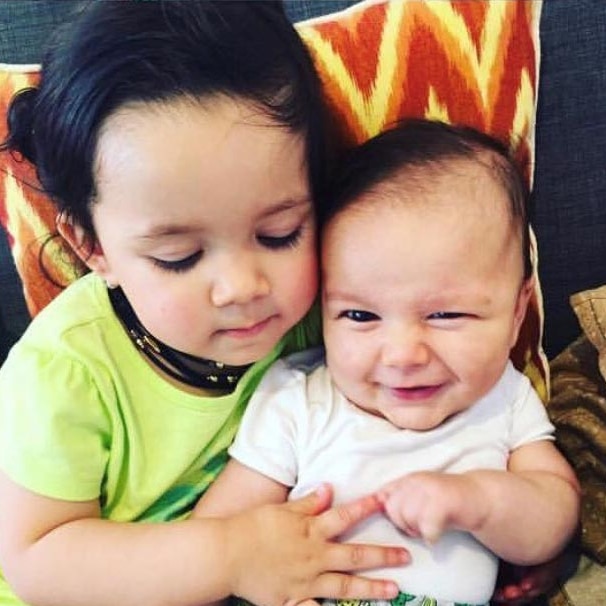 A baby boy is cuddled by his older sister.