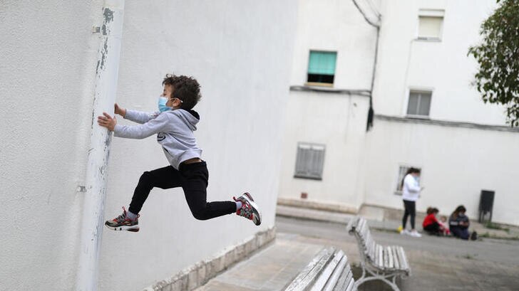 Child is pictured in the middle of jumping up in the air holding the side of a pipe, while wearing a face mask.