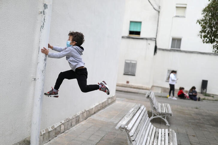 Child is pictured in the middle of jumping up in the air holding the side of a pipe, while wearing a face mask.