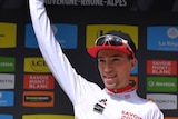 A cyclist wearing a white jersey raises a bunch of flowers on the podium.