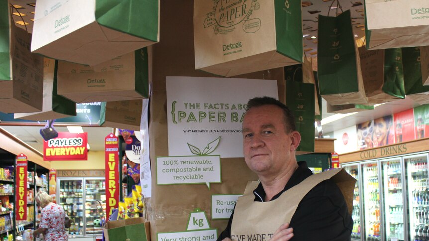 Man standing under a 'tree' of paper bags with aisles of the store visible in the background.