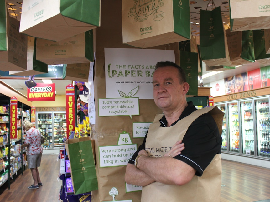 Man standing under a 'tree' of paper bags with aisles of the store visible in the background.