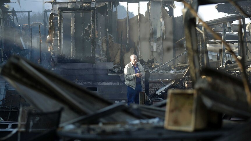 Dick Marsala stands in a beam of light in the middle of his home with just burned beams and small sections of wall left standing