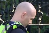 A police officer stands on the footpath making notes on a sunny day.