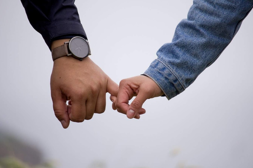 Two people's arms and hands in shot, they are linking pinkie fingers