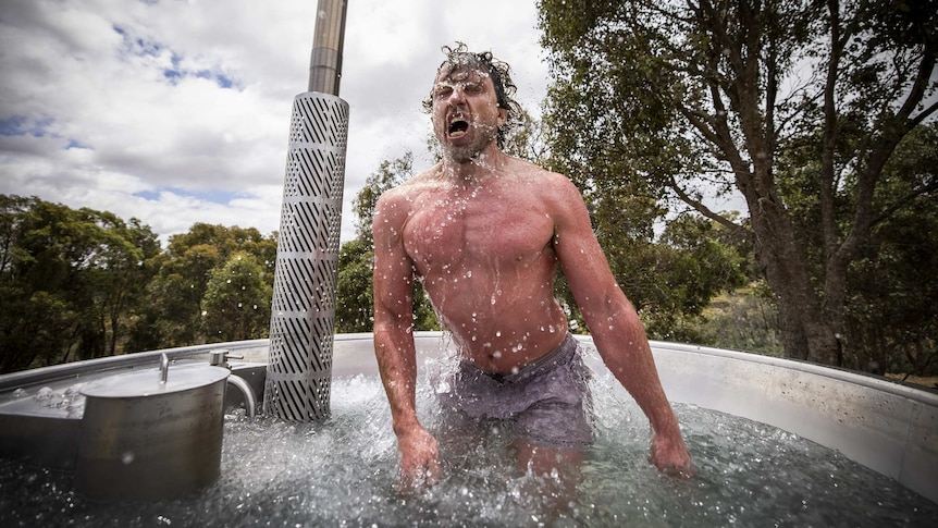 A muscular man flicks water off himself as he emerges from an ice bath