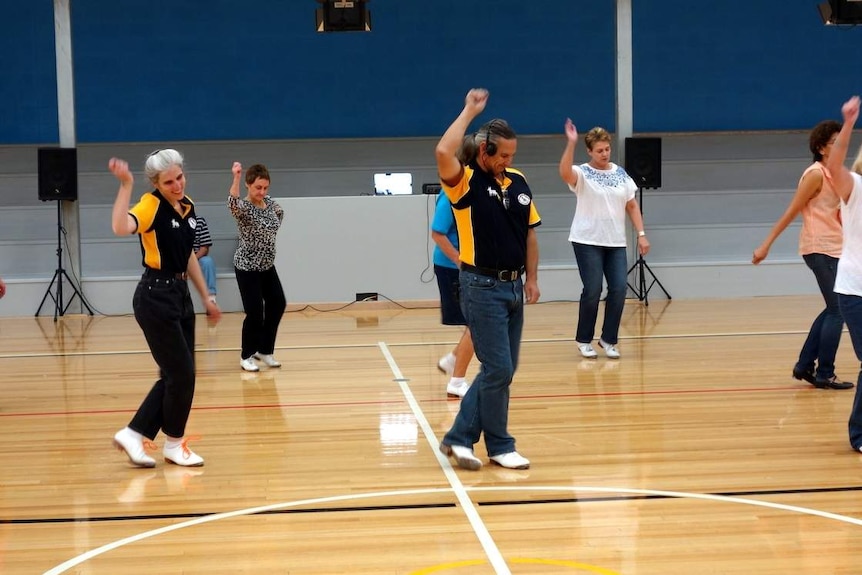 People dancing in rows in white shoes in a gymnasium