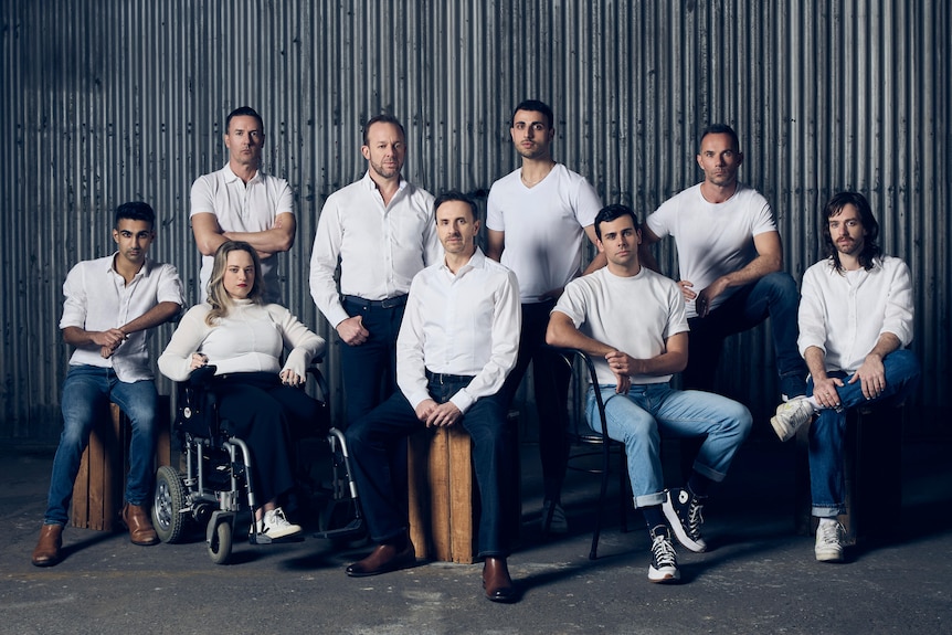 A group of people sitting down in front of a corrugated iron wall