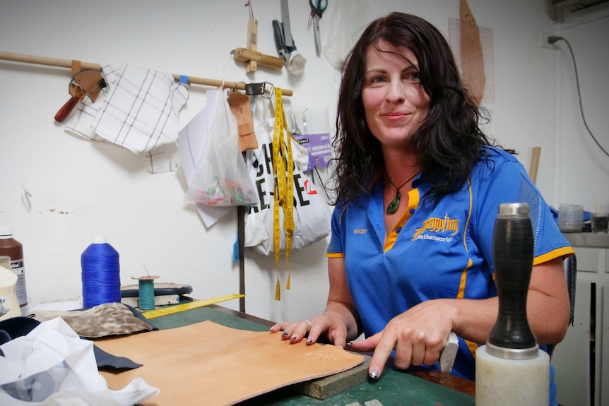 A woman with dark hair sitting at a desk with tools and a sample of brown leather in front of her