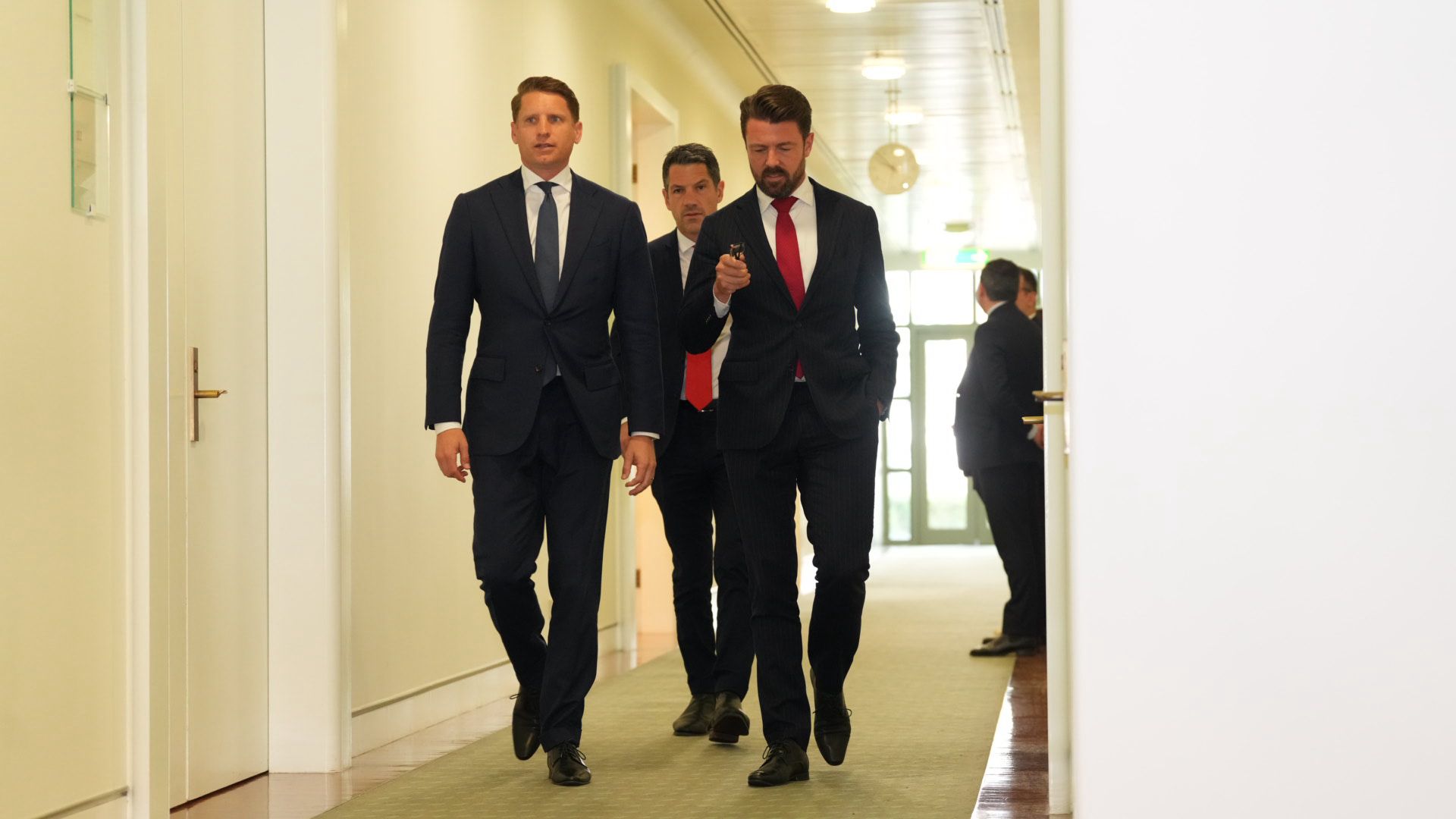 Hombres con trajes oscuros caminan por un pasillo.
