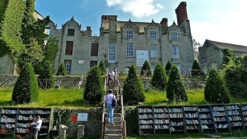 On a bright blue day, you look up at a castle ruin with a single row of bookshelves lining the perimeter wall in the foreground.
