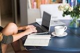 a person types at a laptop on her desk at home, a diary and cup of tea beside her