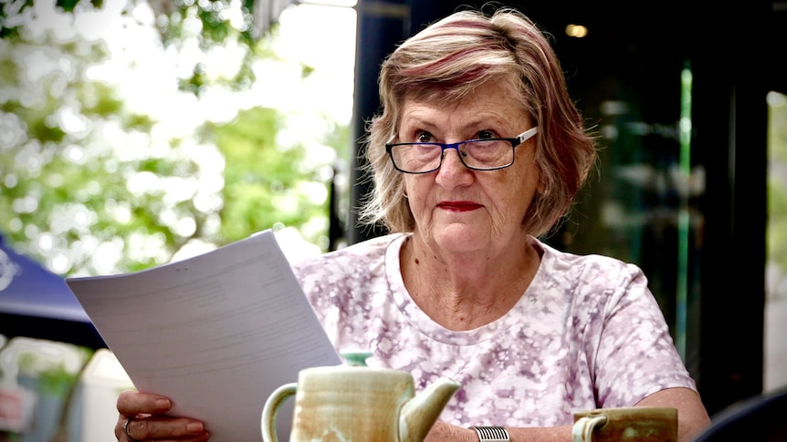 A woman in her sixties reads a document at a cafe 