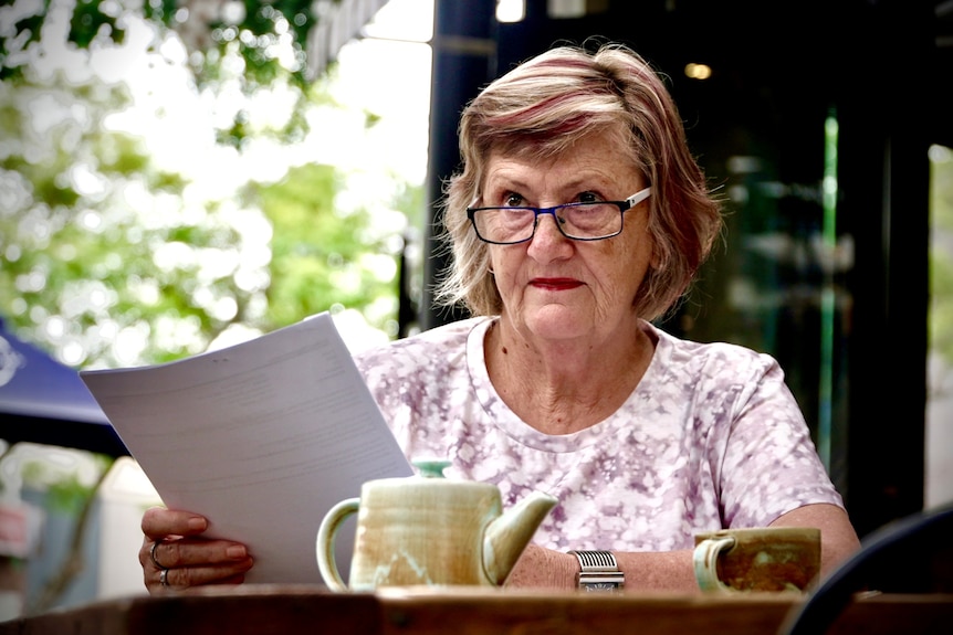 A woman in her sixties reads a document at a cafe 