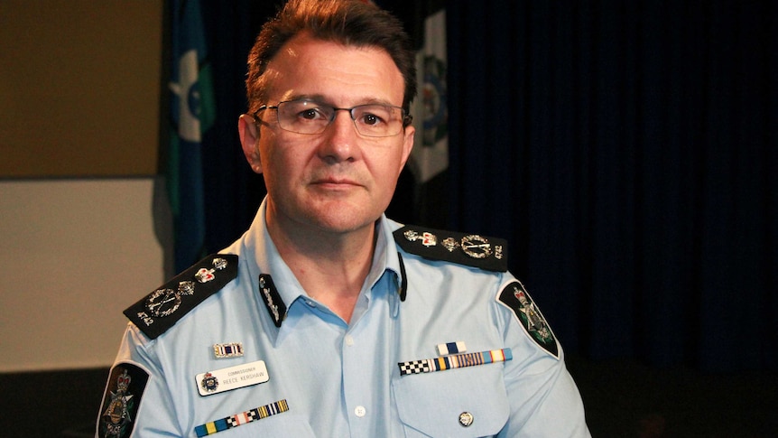 AFP Commissioner Reece Kershaw, in a uniform with flags hanging behind him in a room, looks seriously at the camera.