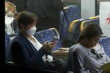 Commuters sit on a train while wearing face masks, some looking at phones, in Sydney
