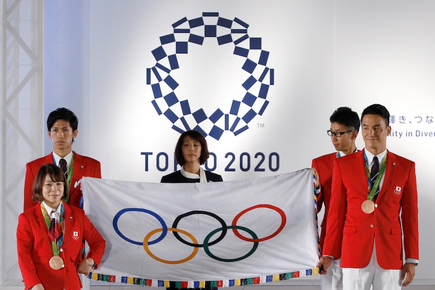 Japanese Olympians hold the Olympic flag during the Olympic and Paralympic flag-raising ceremony.