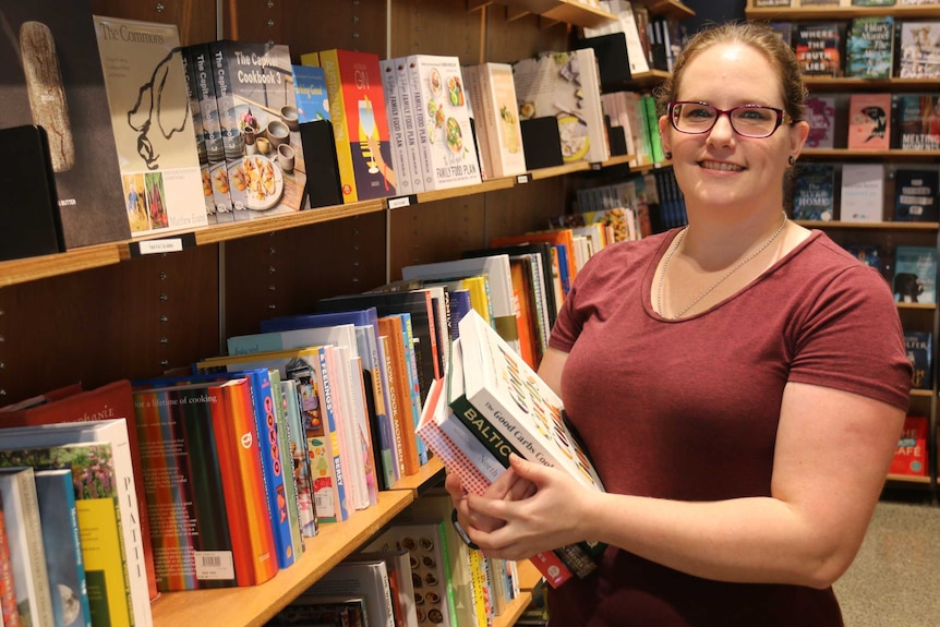Jess holds some books in her shop, smiling.