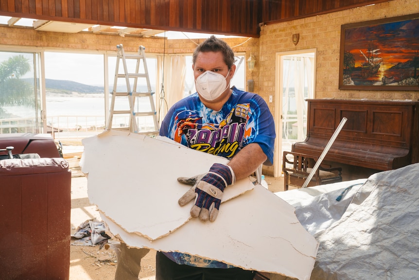 A man wearing a mask and carrying a piece of wall fallen from his house