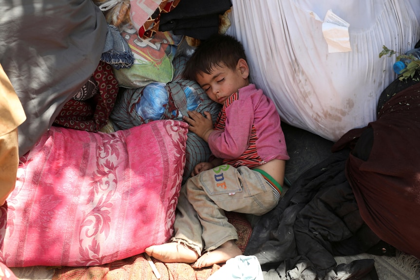 A young boy curls around a plastic bag full of clothing, personal items and sleeps 