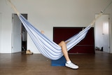 A hammock hangs in a large empty room with a person's leg visible out the side of it for a story on share housing.