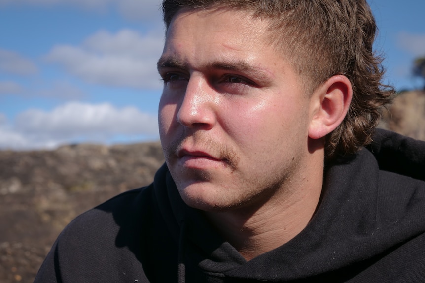Close up portrait of young man with serious expression with the sky and mountains in the foreground. 