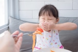 A child covering their mouth, refusing to eat something. 