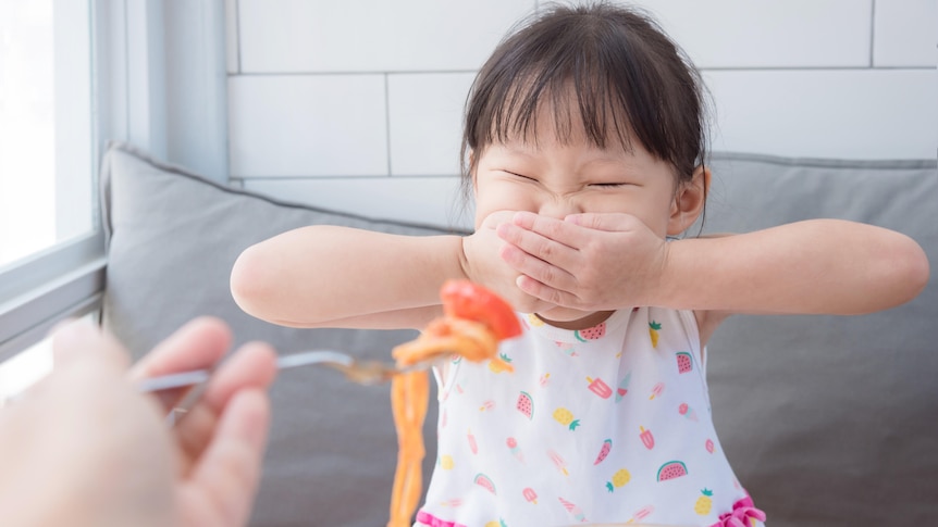 A child covering their mouth, refusing to eat something. 