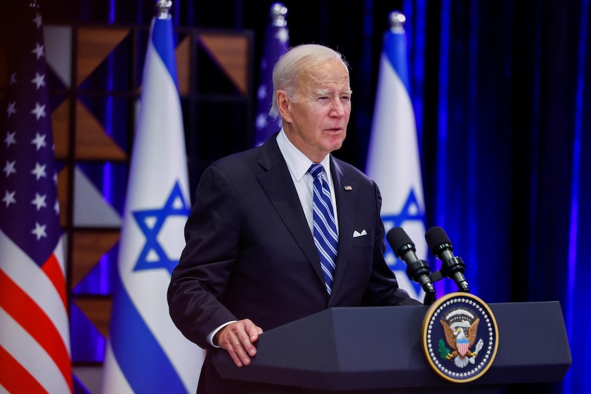 Joe Biden speaks at a podium with Israeli and American flags behind him.