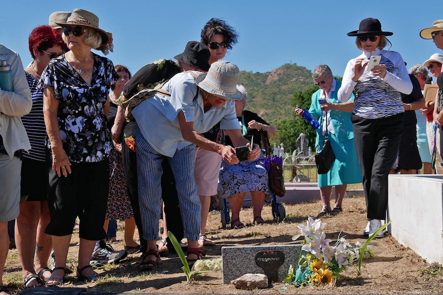 Groups of people crowd around the gravesite of Annie Ferdinand, some are taking photos with their phones.