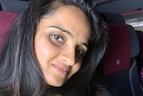 A woman with dark hair wearing a yellow shirt smiles as she sits on a plane next to her daughter.