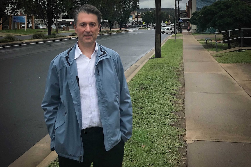 A man stands in the main street wearing a blue coat and white shirt