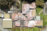 An aerial photo of a series of burnt buildings surrounded by large trees and lawn.