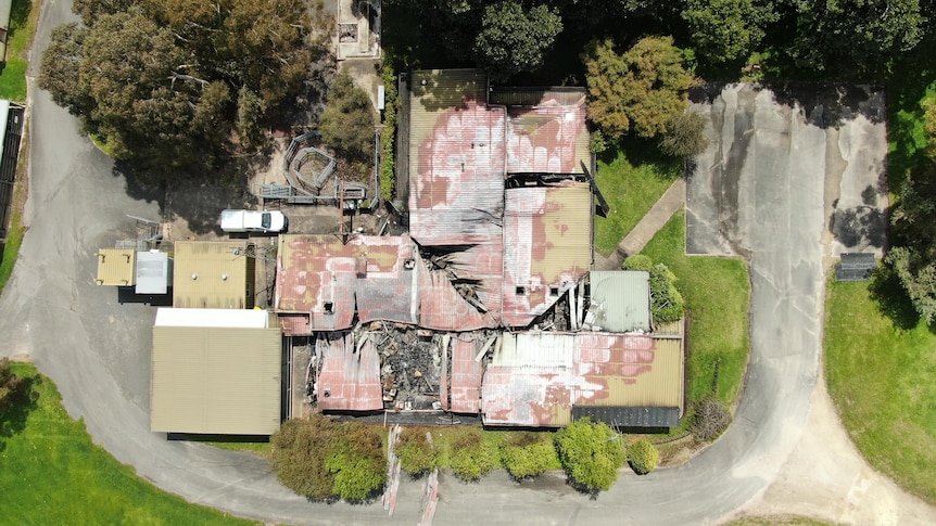 An aerial photo of a series of burnt buildings surrounded by large trees and lawn.