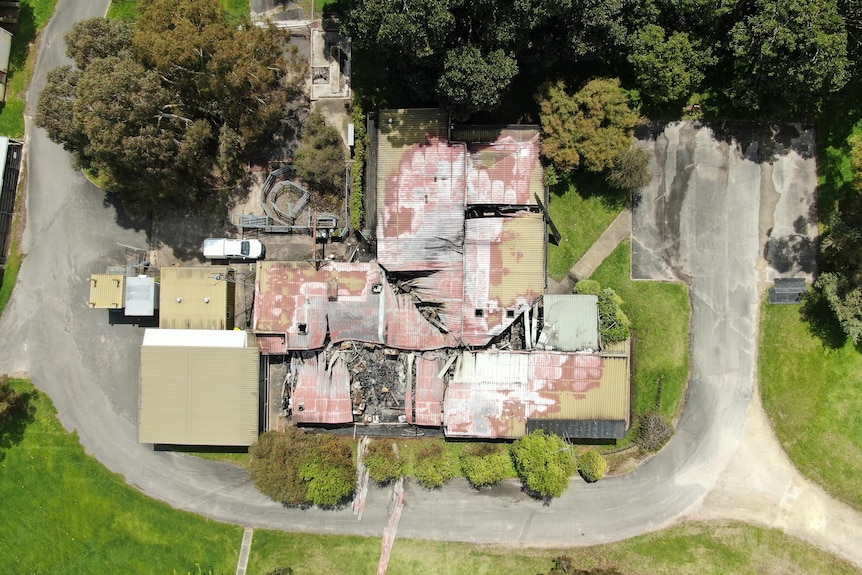 An aerial photo of a series of burnt buildings surrounded by large trees and lawn.