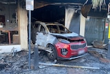 A burnt-out red car in the entrance of a tobacco shop.