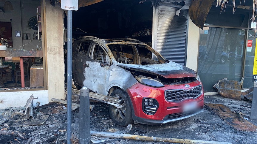 A burnt-out red car in the entrance of a tobacco shop.