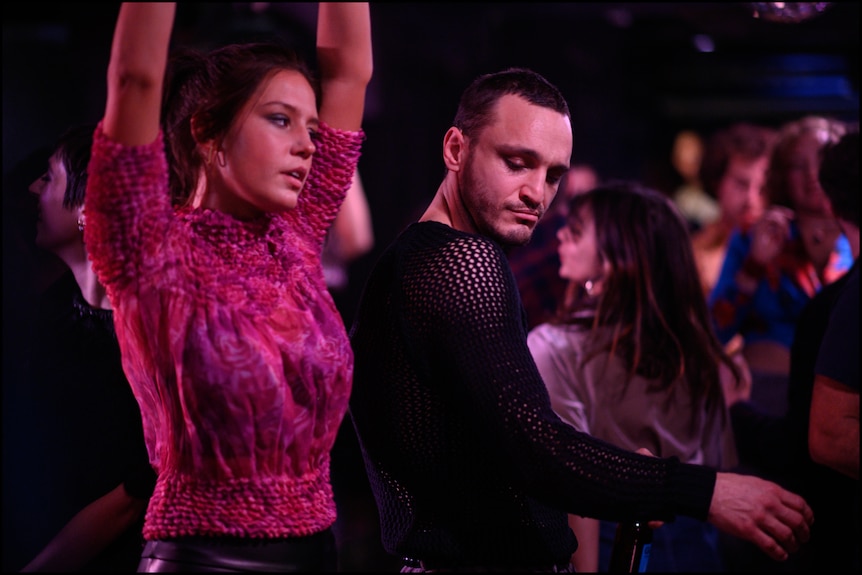Adèle Exarchopoulos, a brunette white woman in pink top, and Franz Rogowski, a brunette white man in black top, dance in a club.