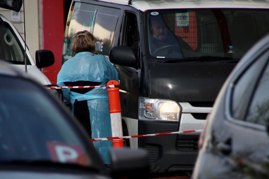 A woman dressed in blue at the window of a van with a man inside.