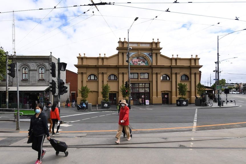 People wearing masks cross the street in front of the Queen Victoria Market in Melbourne.