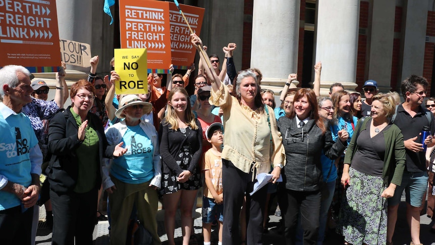 A group of people outside the WA Supreme Court, some carrying signs, celebrate the court's decision on Roe 8.