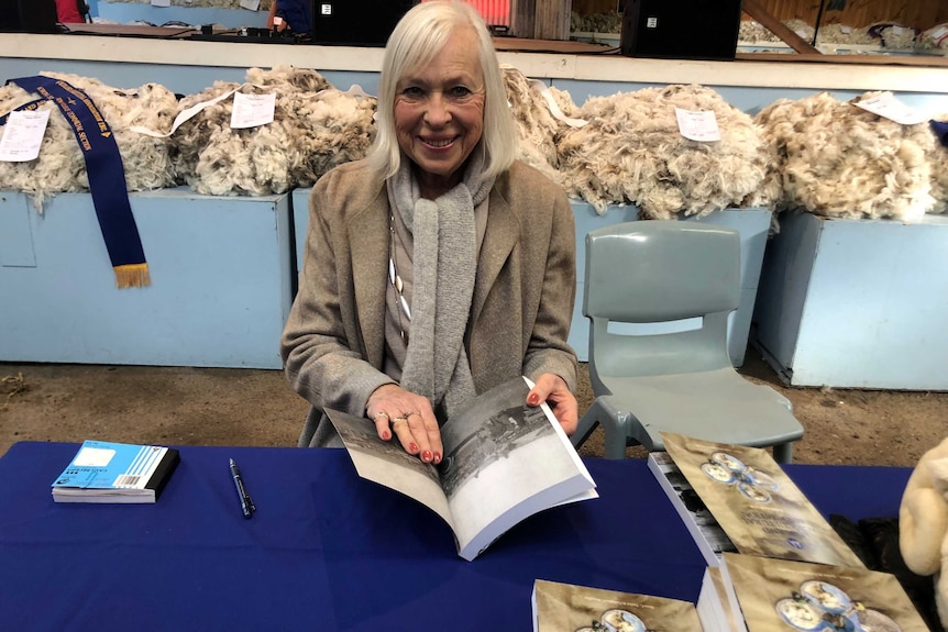 an author sits with her book open in front of piles of wool