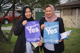Two women pose for a photo holding placards