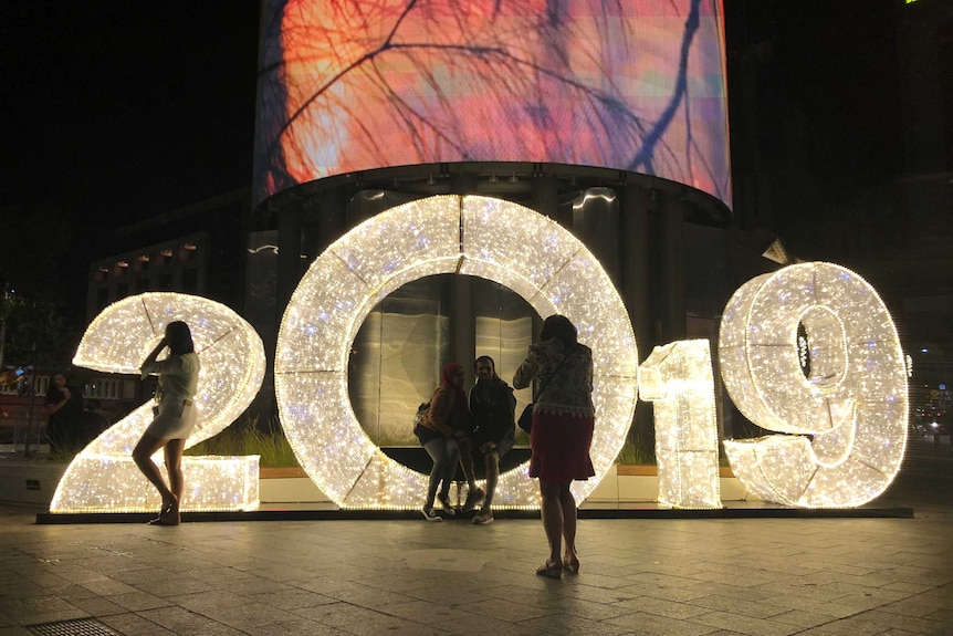 People take photographs near a large 2019 sign lit up at Yagan Square.